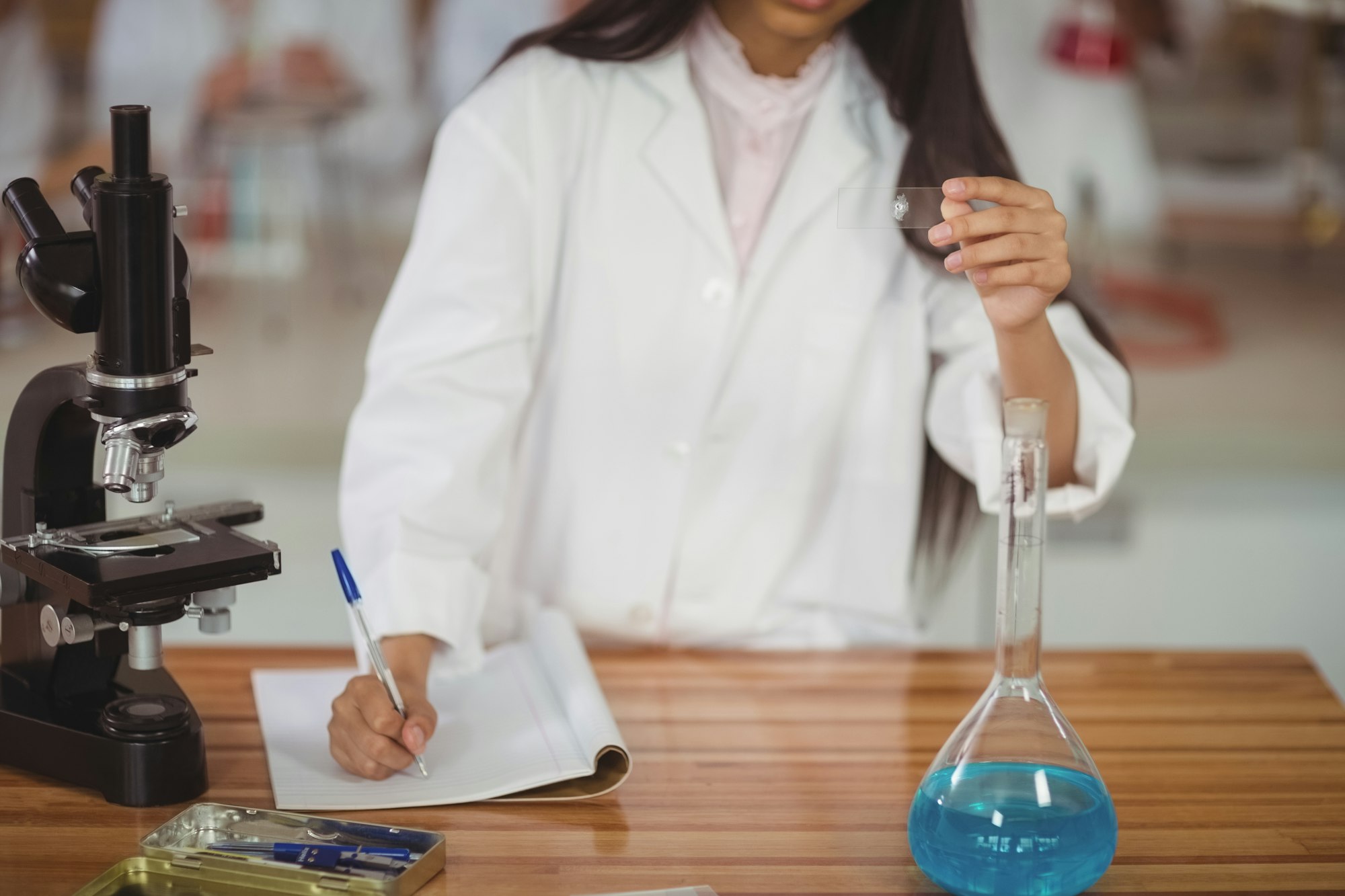 School girl writing in journal book while experimenting in laboratory