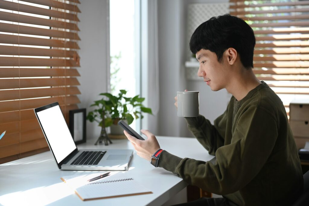 Side view of young businessman drinking coffee an checking social media on mobile phone.