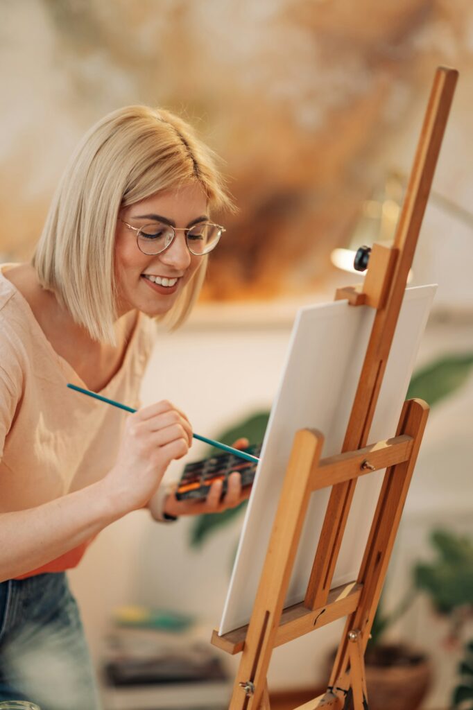 Smiling creative female author painting on canvas at art studio.