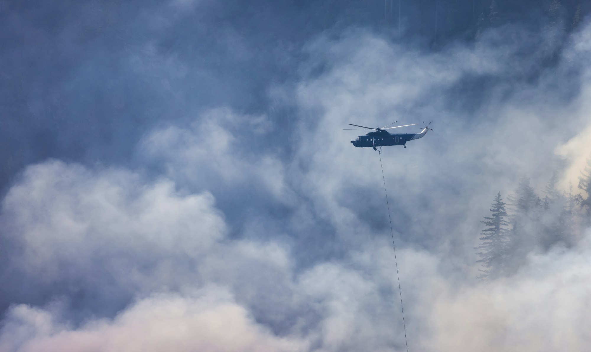 Wildfire Service Helicopter flying over BC Forest Fire and Smoke on the mountain near Hope