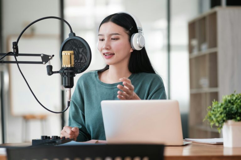 A woman is sitting at a desk with a laptop and a microphone