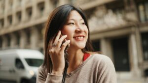 Asian woman talking on smartphone discussing latest news with friend outdoors