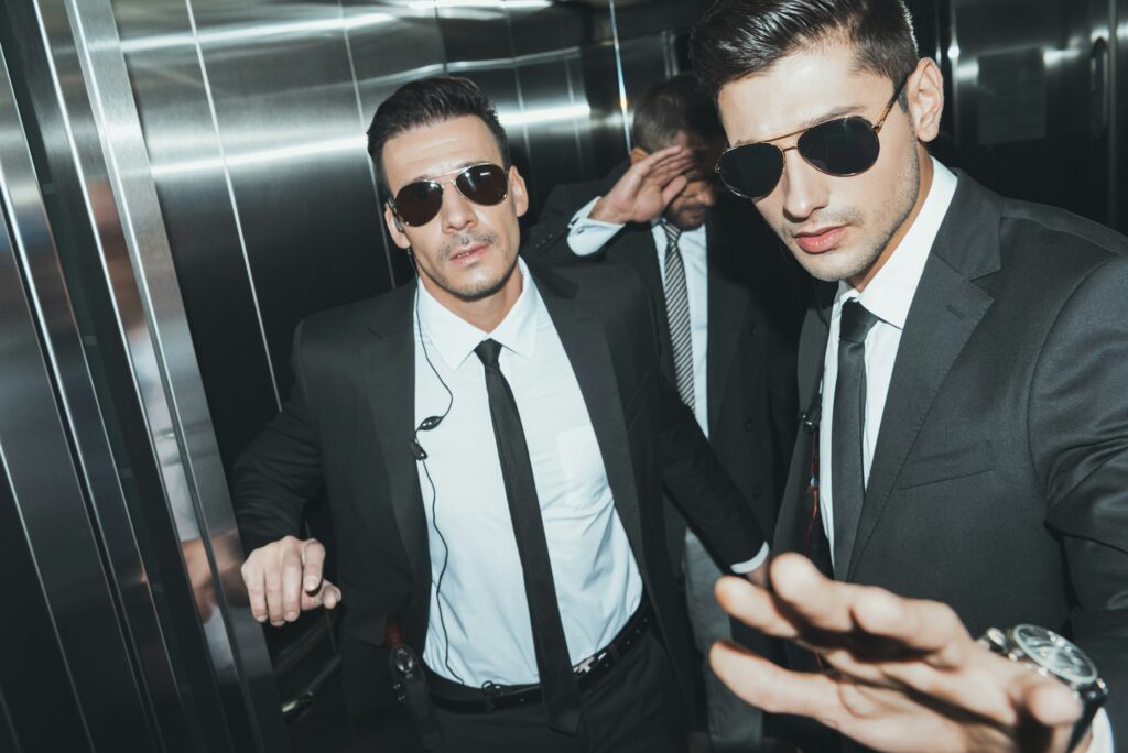 bodyguards stopping paparazzi and celebrity covering face with hand in elevator