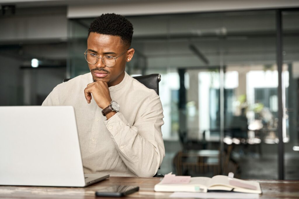 Busy African business man thinking on online investment working on laptop.