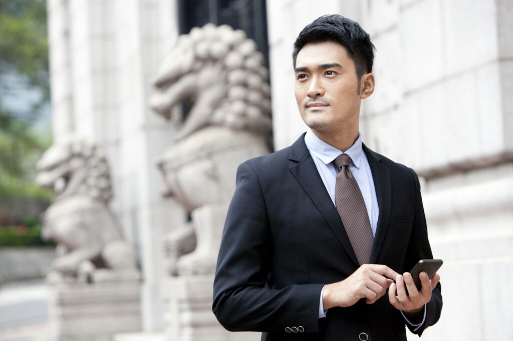 Confident businessman with smart phone outside a building, Hong Kong