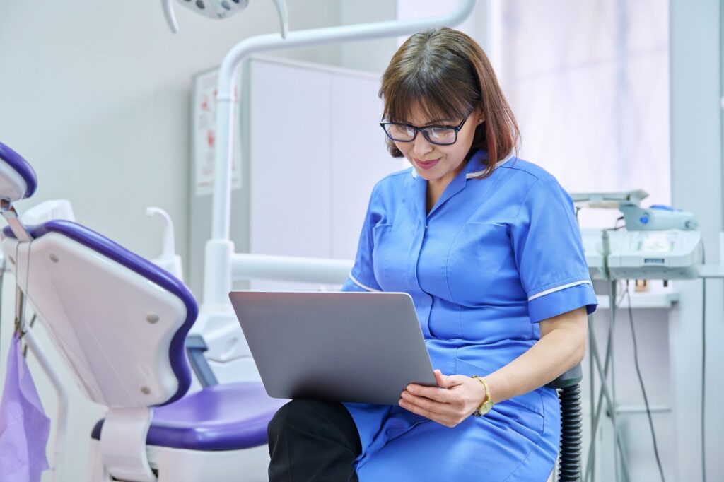 Doctor nurse dentist sitting in the office using a laptop.