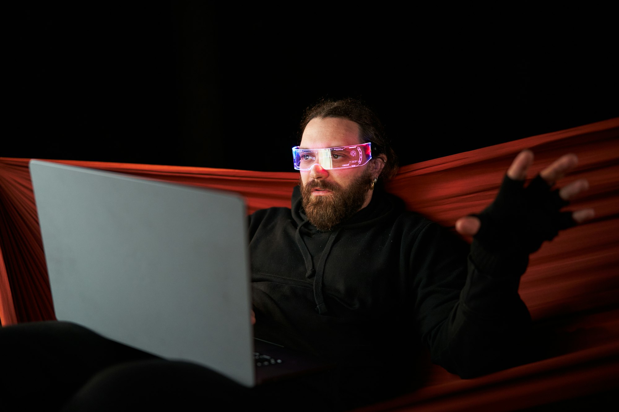 Gamer using a laptop and a extended Reality goggles while sitting on an hammock at night