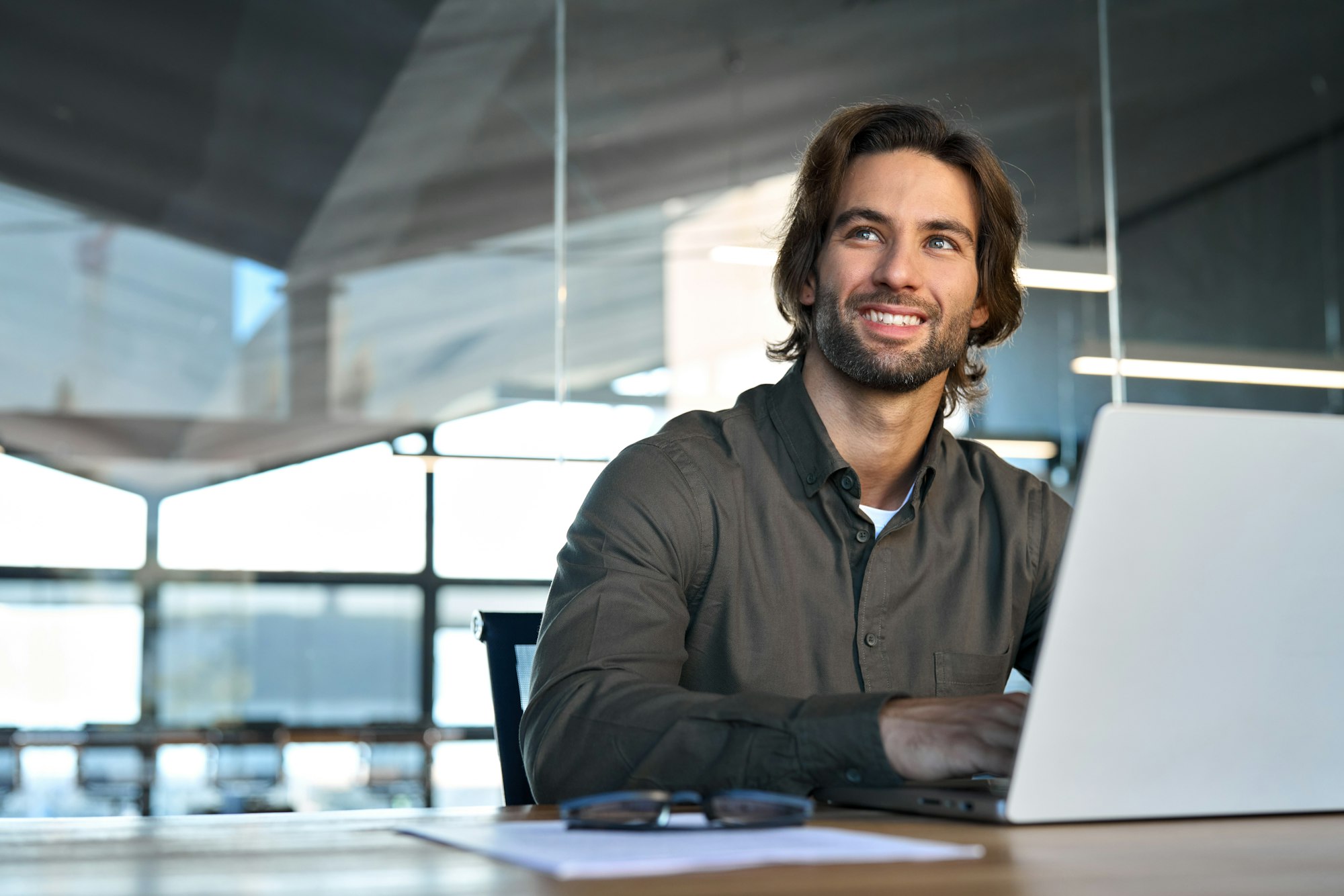 Happy young European business man employee looking away using laptop at work.