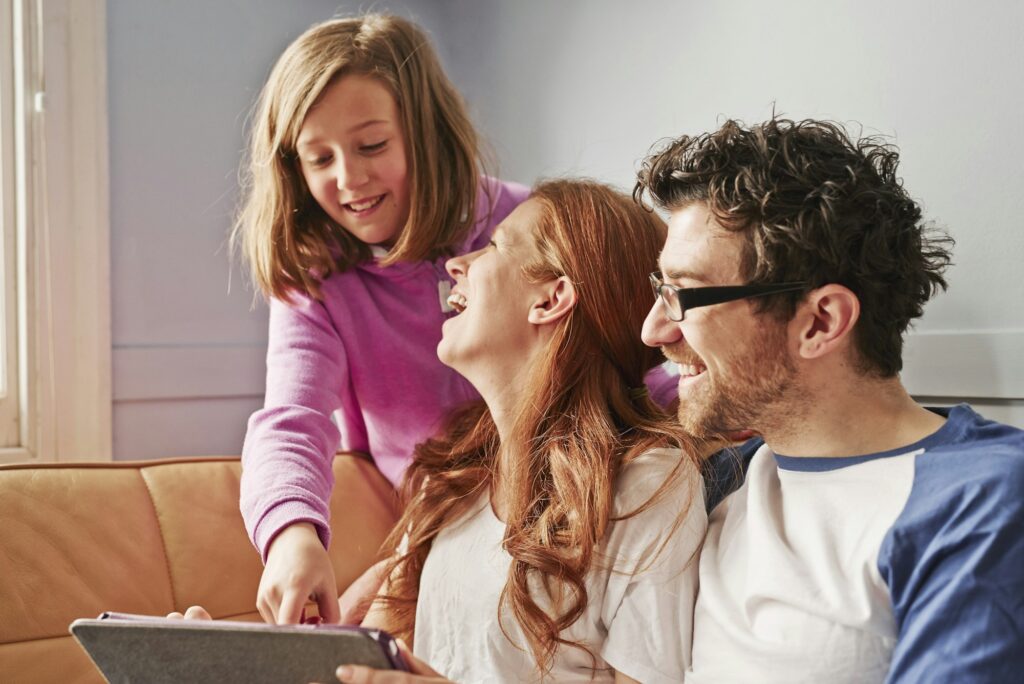 Mid adult parents and daughter on sofa looking at digital tablet