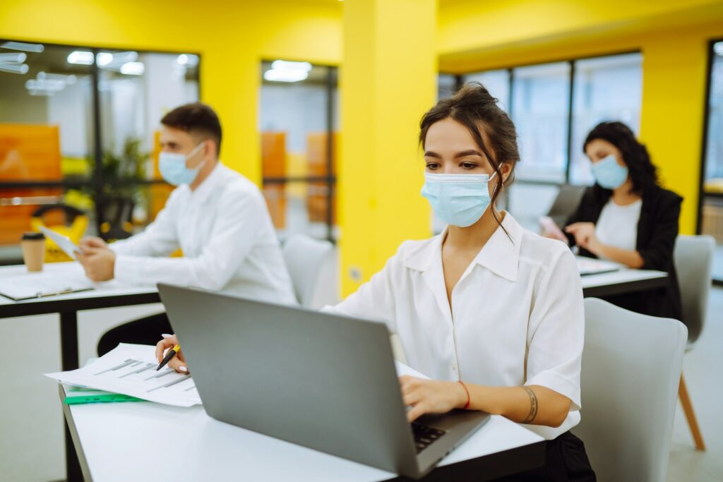 Office worker wearing face mask for social distancing for virus prevention while using laptop.