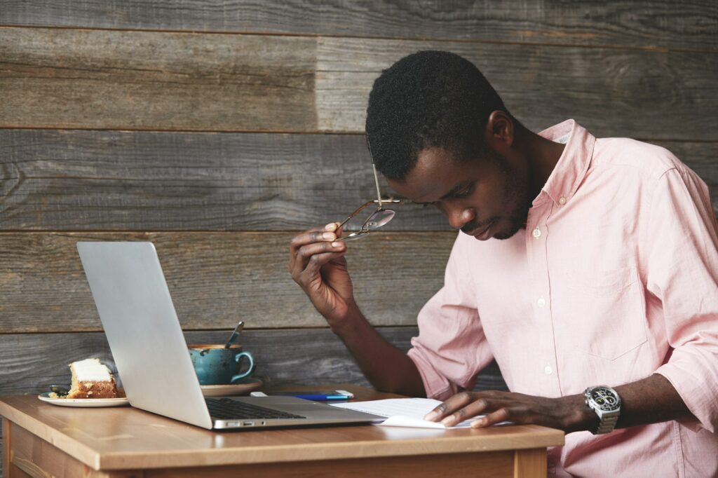 Portrait of thoughtful and concentrated young African American copy-writer, dressed in pink shirt, w