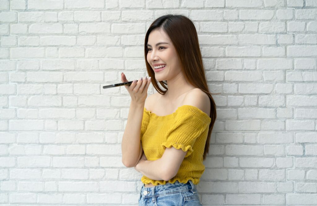 Smiling Asian woman holding phone speak activate virtual digital voice assistant on smartphone.