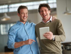 Two male coworkers sharing something humorous on a digital tablet