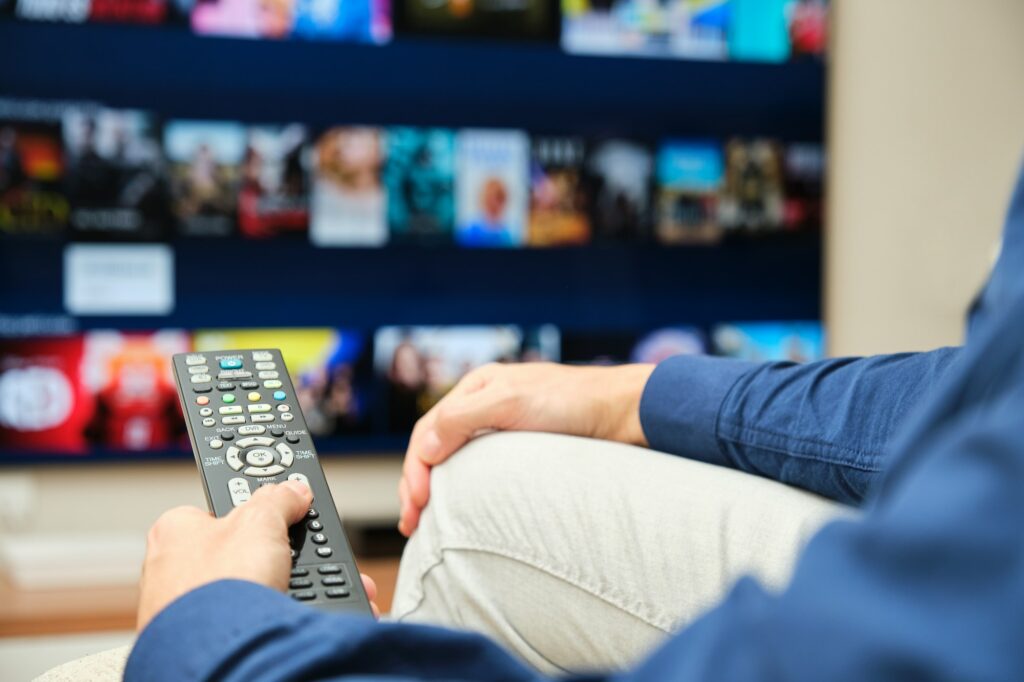 unrecognizable man sitting on the sofa looking on the tv for content on a streaming platform