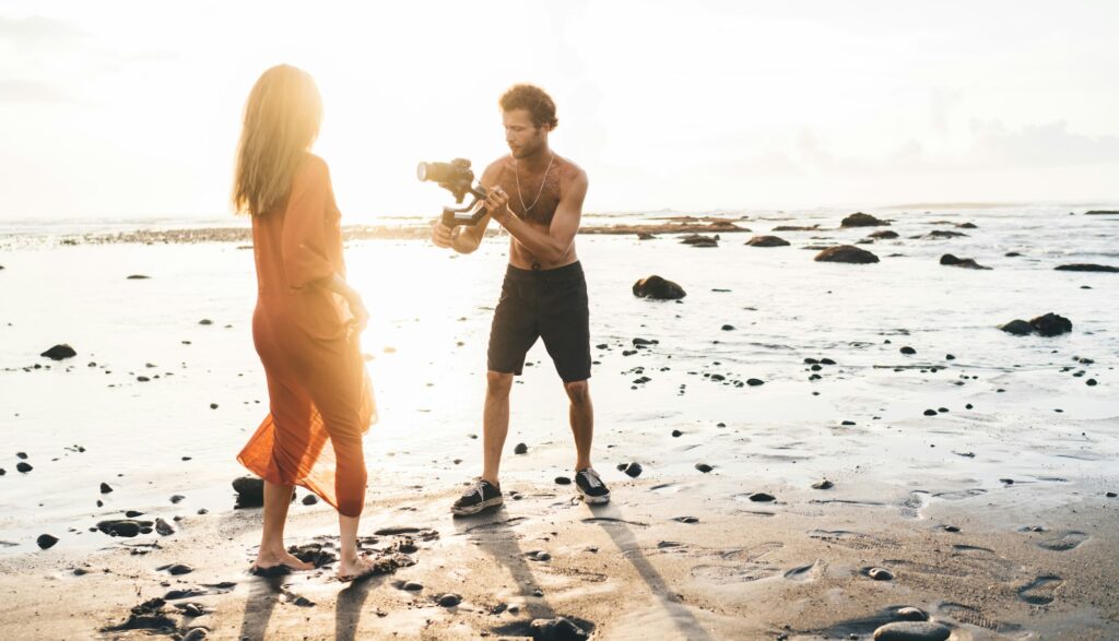 Video maker shooting fashion video with slender model on beach