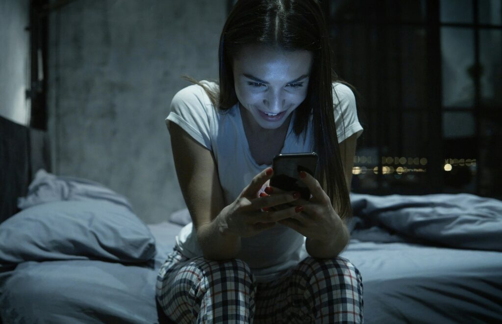 Young attractive woman chatting via smartphone at night using dating app