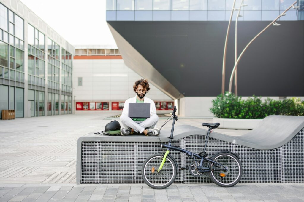 Young man working on laptop outdoors, next to bicycle - Tech Freelancer in the city