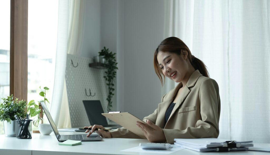 Attractive young woman sitting and her workplace and checking information on clipboard.