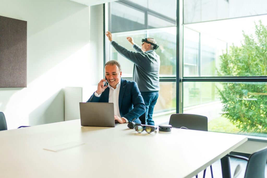 Businessman using laptop while colleague using VR googles in office