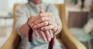 Hands, cane and sofa in home for senior person with disability, mobility and recovery from stroke.