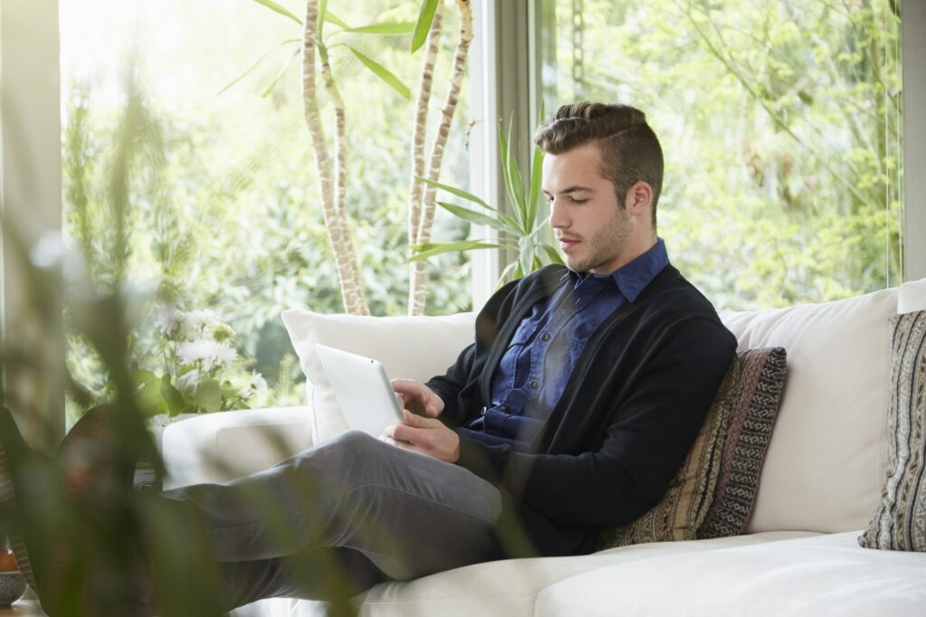 Man relaxing on sofa with feet up looking at digital tablet