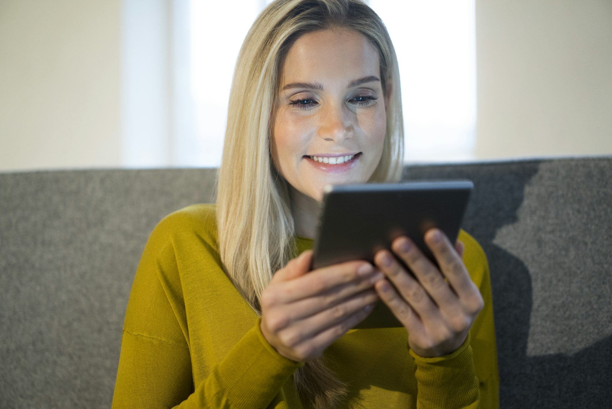 Portrait of smiling woman sitting on couch using mini tablet