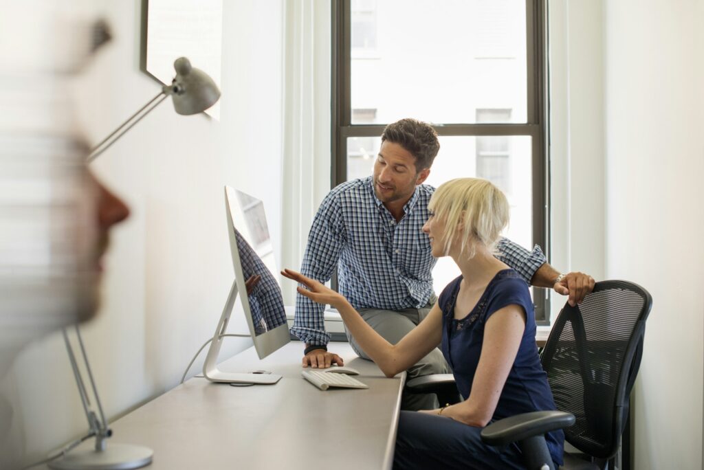 Three business colleagues in an office, two talking and one standing by the door.