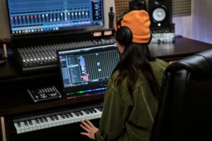 Young woman, female artist looking focused while playing keyboard synthesizer, sitting in recording