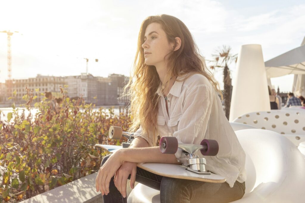 Young woman with skateboard relaxing by river, Berlin, Germany