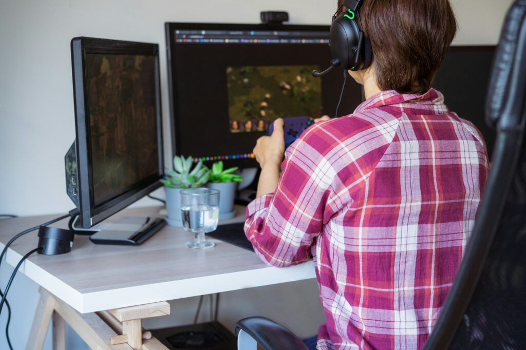 Back View Woman in a headset with Xbox controller playing online games on her desktop pc