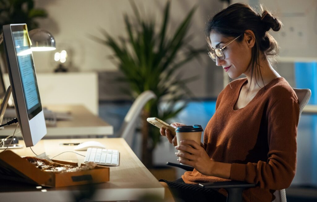 Beauty business woman sending messages with mobile phone while working with computer in the office.