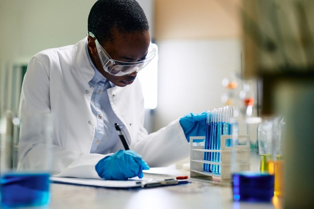 Black female scientist writing data during medical research in laboratory.