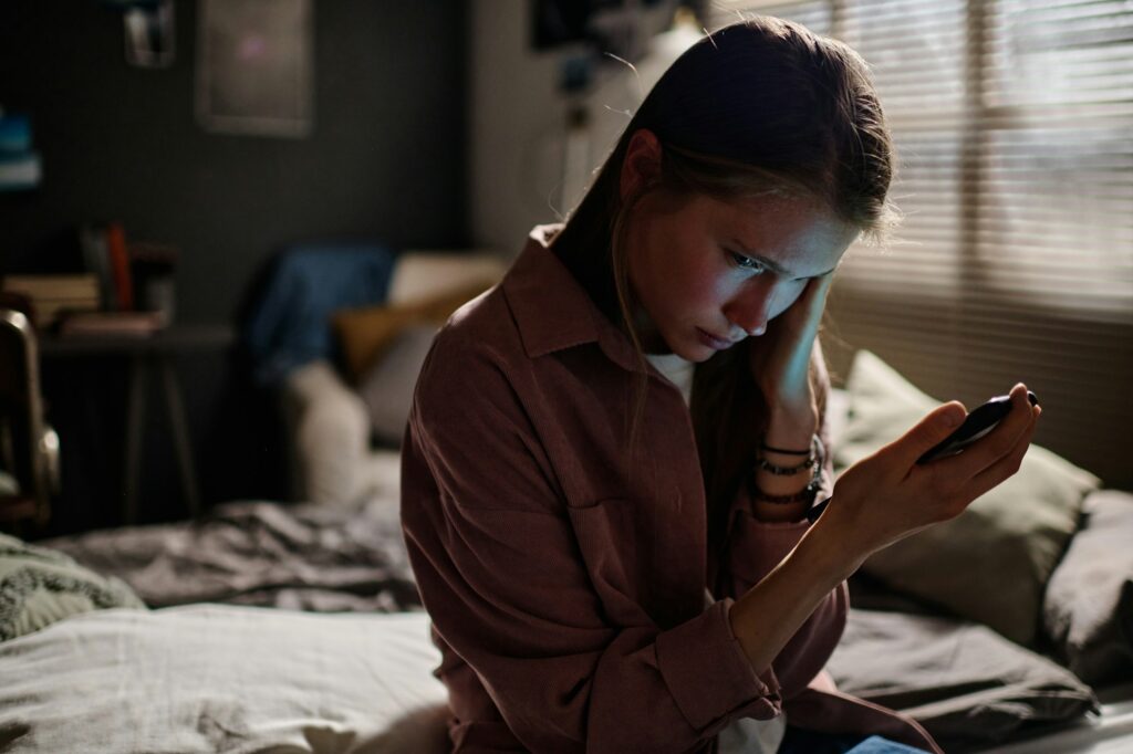 Offended girl with smartphone suffering from night and day cyberbullying