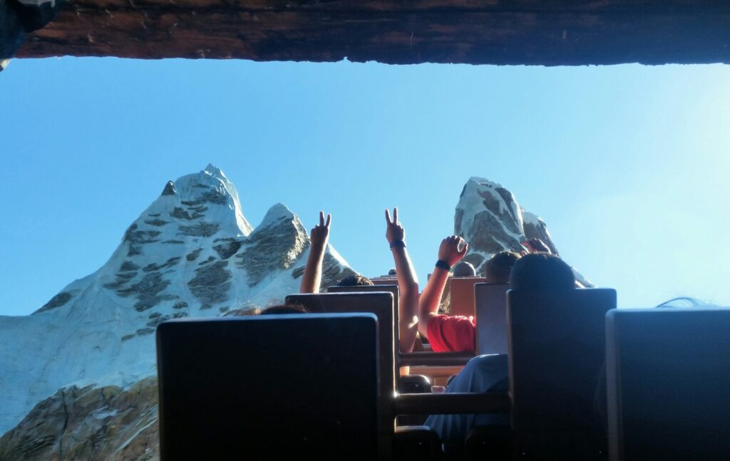 People on rollercoaster ride at Disney world scream and hold up hands at the top.