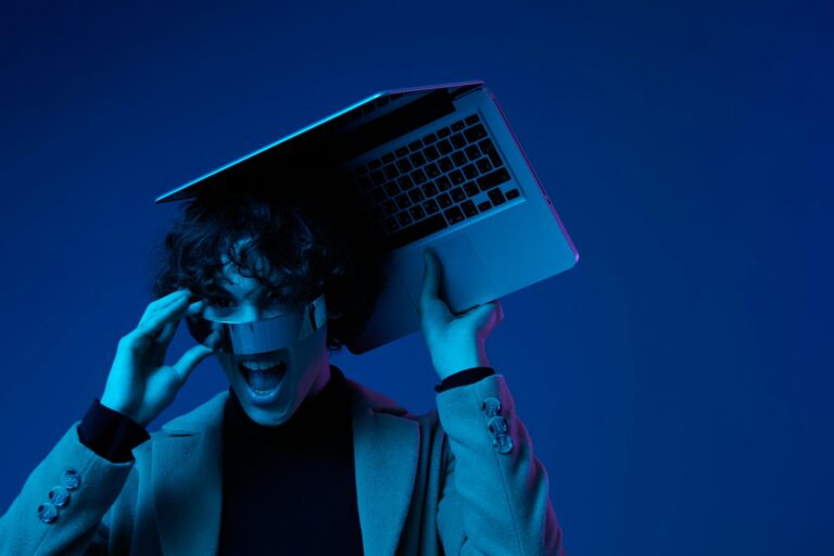 Portrait of stylish man hacker with laptop and futuristic glasses in blue light, cyber security