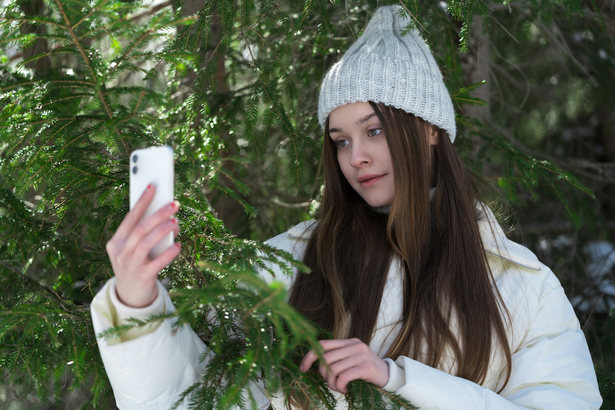 Portrait of teenager girl 17 year old using cellphone on pine forest, holding smartphone in hand