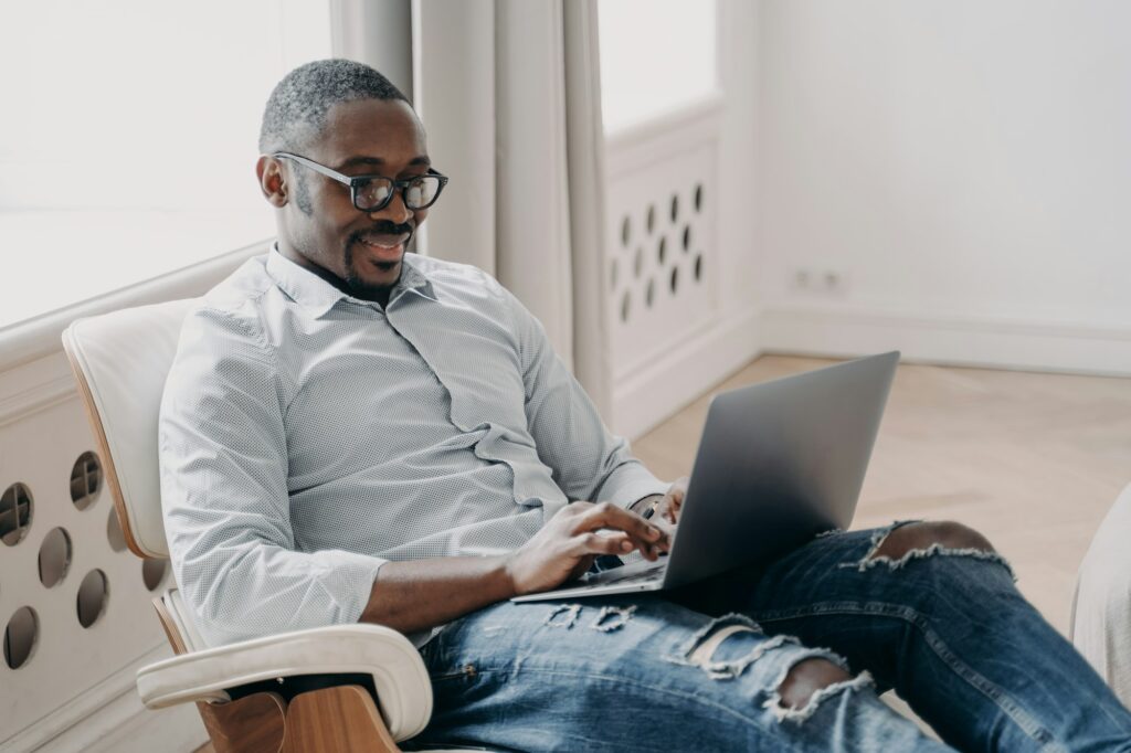 Relaxed businessman in casual attire browsing laptop while reclining comfortably.