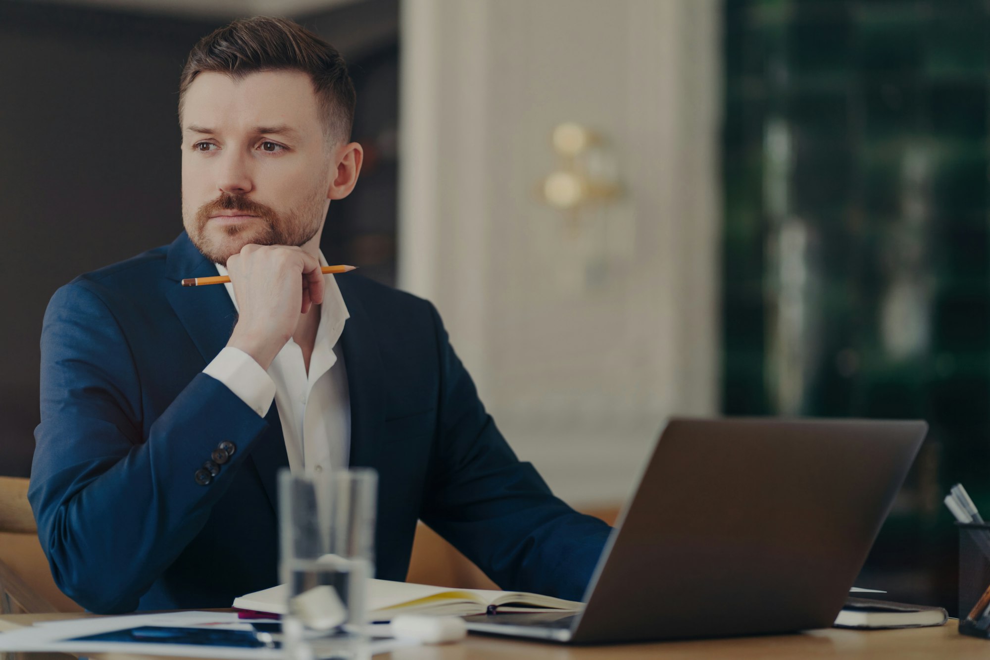 Serious male entrepreneur in blue suit, stylish office, thinking about business challenges