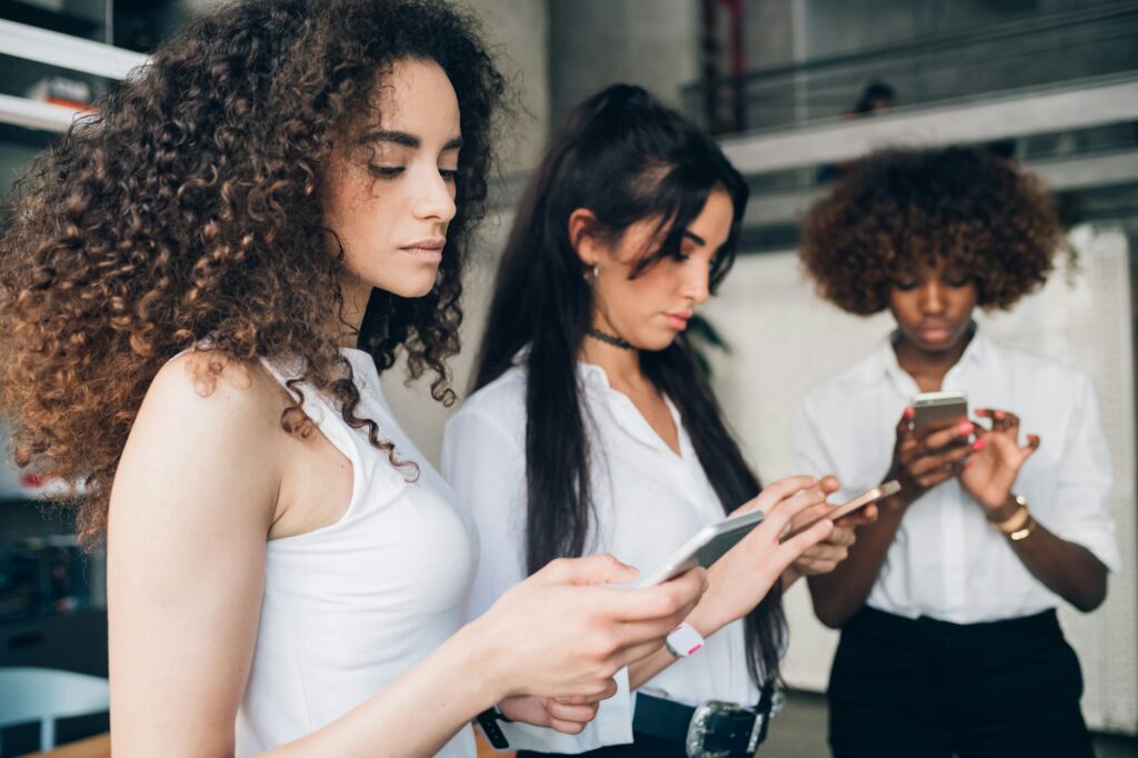 three young businesswomen checking and sharing data with smartphone