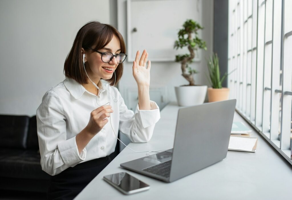 Young Businesswoman Video Calling On Laptop Waving Hello In Office