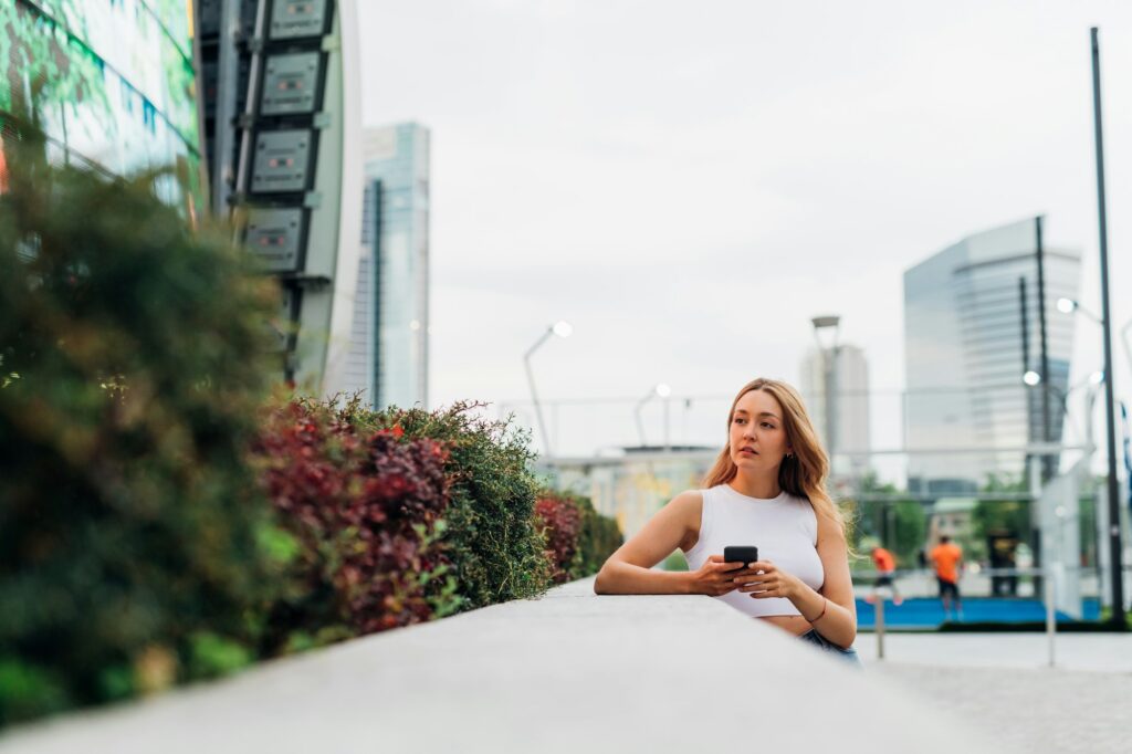 Young caucasian woman using smartphone looking over positive and trustful in future