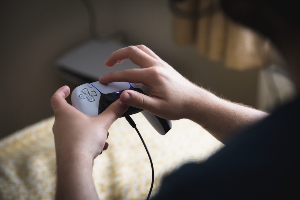 Boy holding a PlayStation 5 video game controller and using the joypad to play games indoors