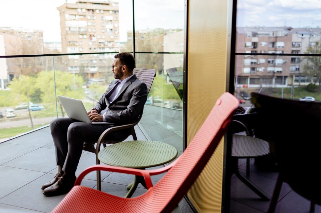 Business Professional Engrossed in Work on a Laptop at a Modern Urban Office Balcony.