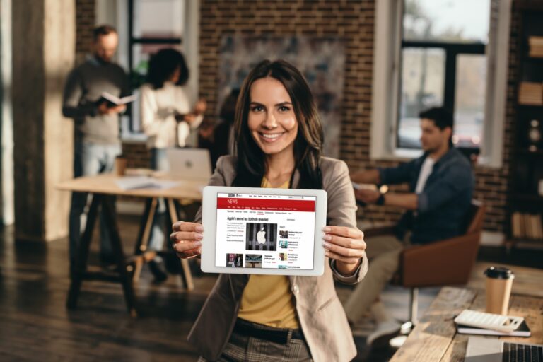 happy casual businesswoman holding tablet with bbc news website on screen in loft office with