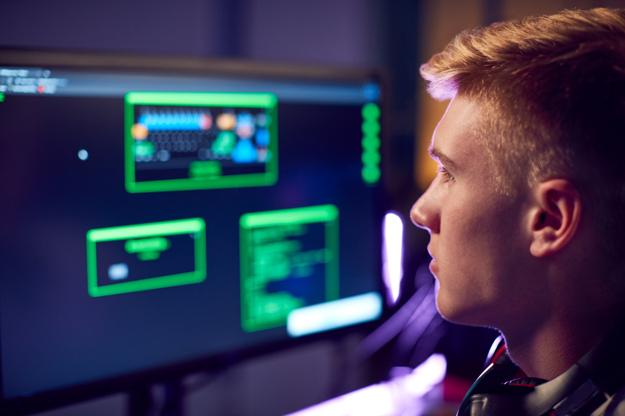 Male Teenage Hacker Sitting In Front Of Computer Screens Bypassing Cyber Security