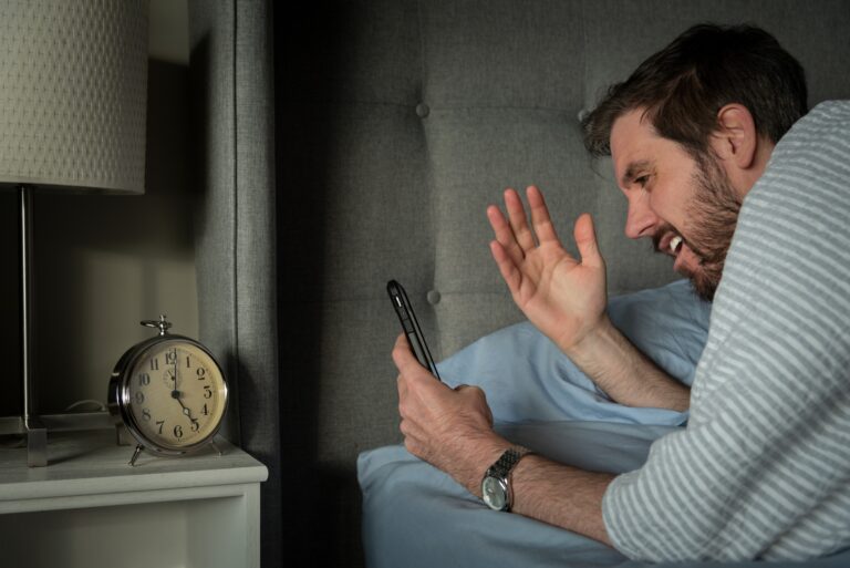 Man reacting to phone screen while waking up in bed