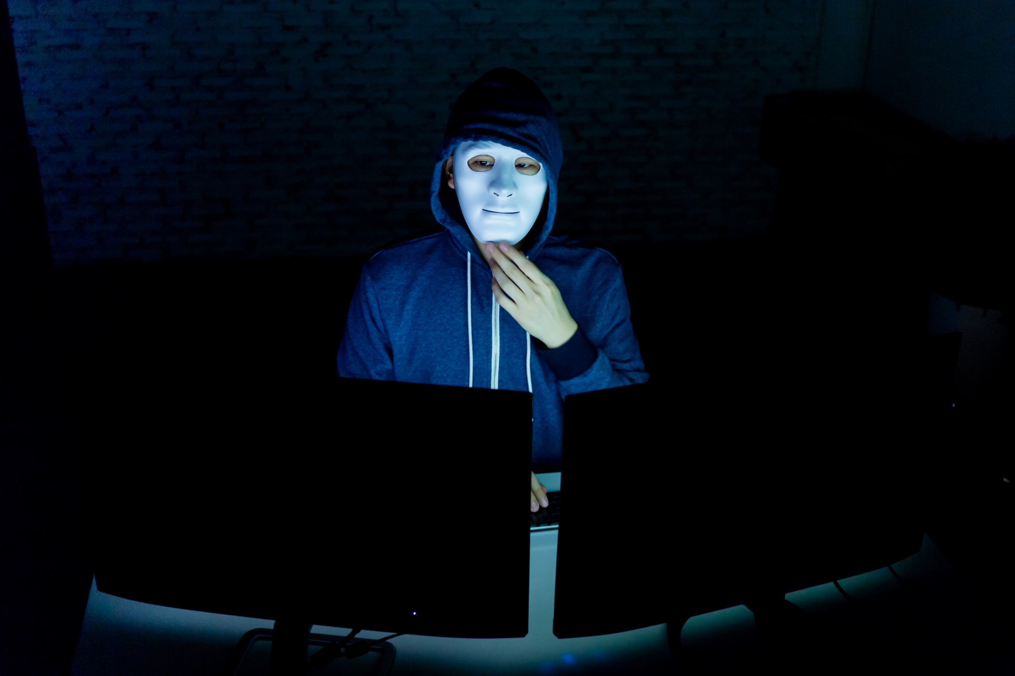 Masked hacker using computer to hack into system and trying to commit computer crime