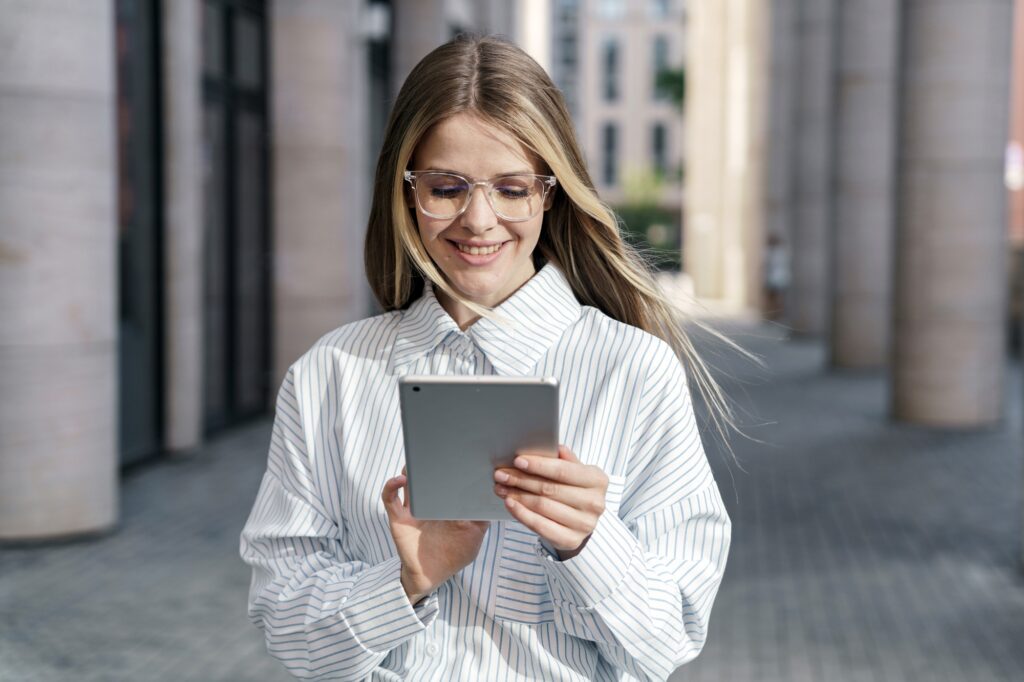 Smiling businesswoman reading on tablet amidst urban columns, embodying modern professionalism.