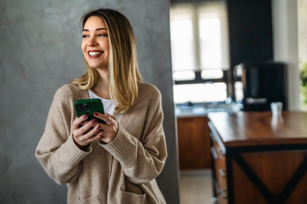 Smiling young woman chatting in social networks, working, using mobile applications at home.