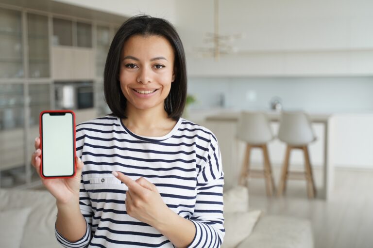 Tenant woman pointing at phone with mock up blank screen reccomends app of renting service at home